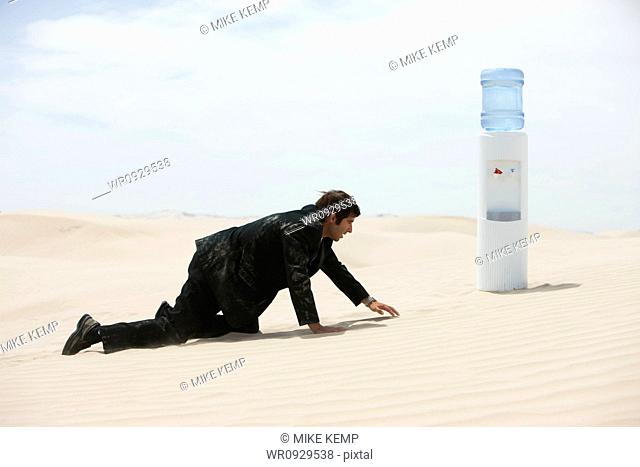 USA, Utah, Little Sahara, mid adult businessman crawling to water cooler on desert