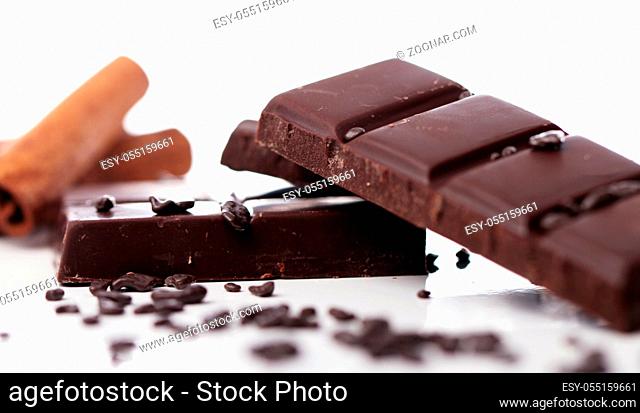 Pieces of chocolate with cinnamon sticks against white background