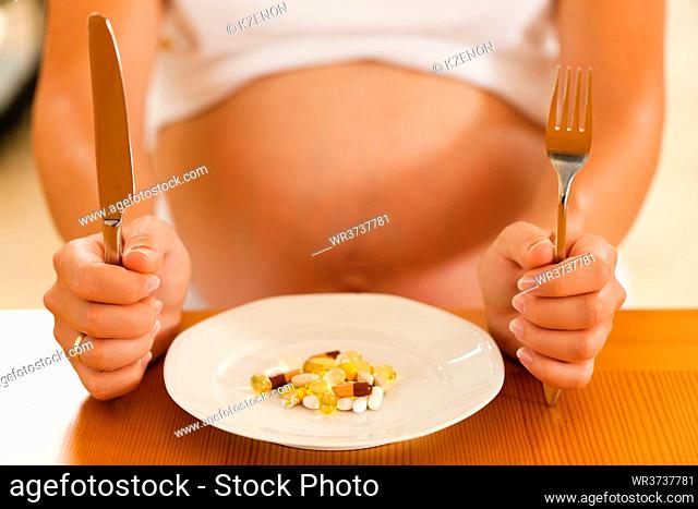 pregnant woman with a plate full of pills and capsules in front of her