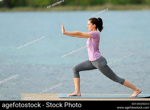 Side view portrait of a woman doing tai chi exercise in a lake pier on summer