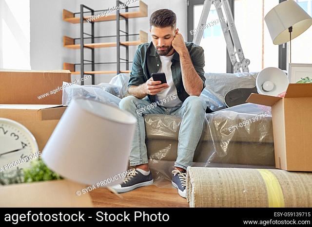 sad man with smartphone and boxes moving home