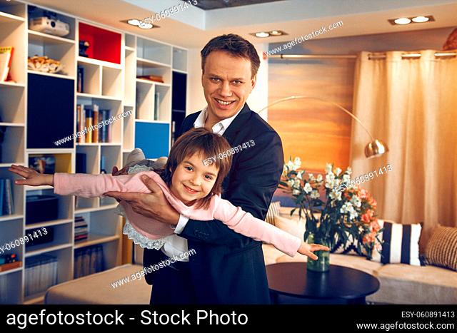 Father businessman standing middle room and holding daughter in hands. Playing together