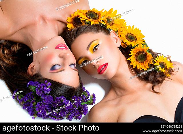 Two beautiful young women with yellow and violet flowers in hair. Bright makeup. Beauty shot. Copy space. Isolated