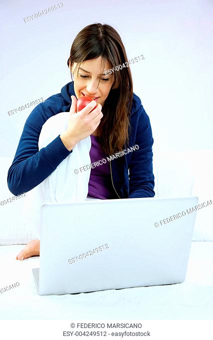 Woman smiling eats apple sitting in front of computer