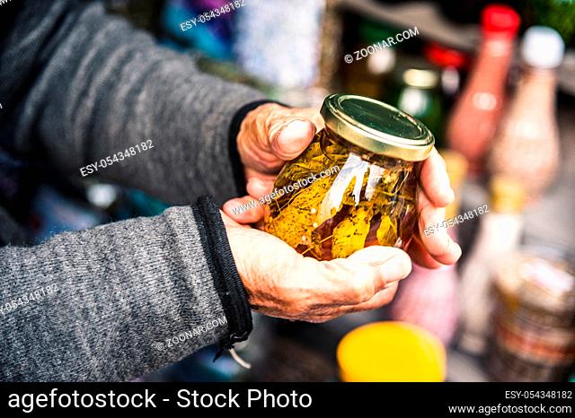 Old wrinkled hands hold a jar with mountain jam from the leaves of Caucasian trees leaves in the mountains