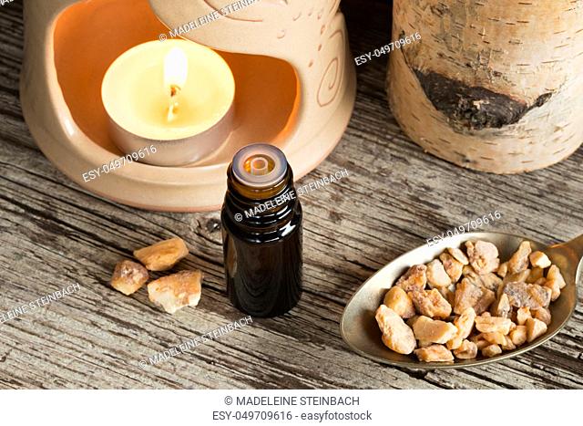 A bottle of styrax benzoin essential oil with styrax benzoin resin and an aroma lamp in the background