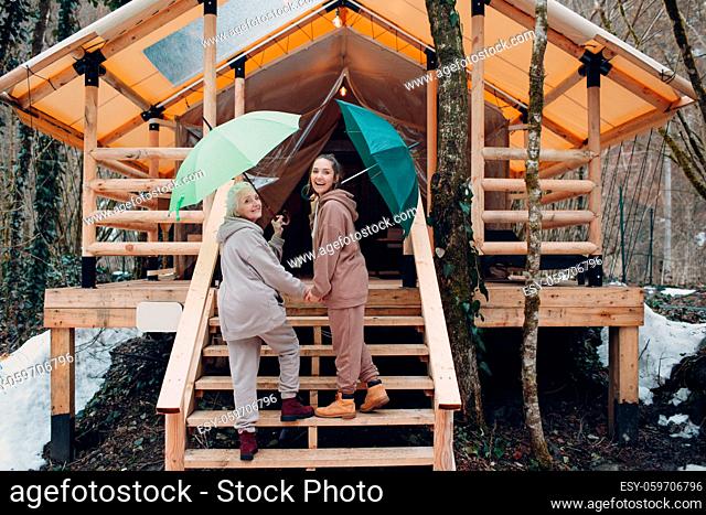Elderly and young adult women with umbrella at glamping camping tent. Modern vacation lifestyle concept