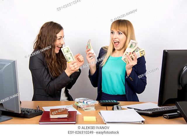 for office table two women collaborators happily hold hands in a pack with the money and express strong
