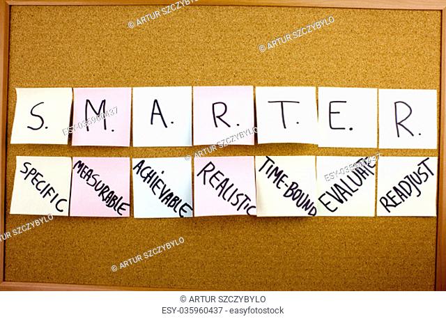 Phrase SMARTER in black ext on a sticky note pinned to a cork notice board specific, measurable, attainable, recorded, timely colorful sticky notes on cork...
