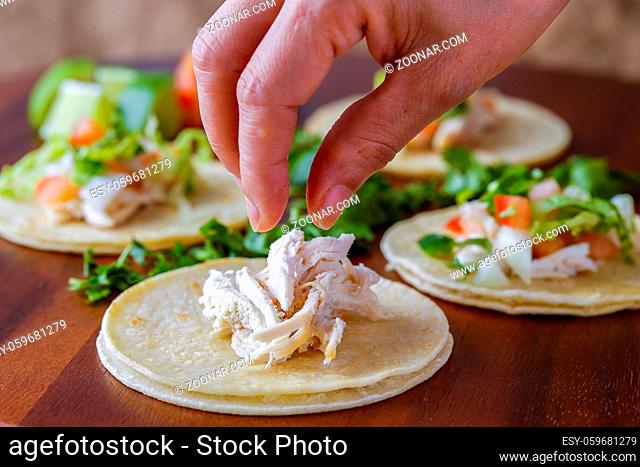 Putting pieces of chicken on a small street taco on a wooden board