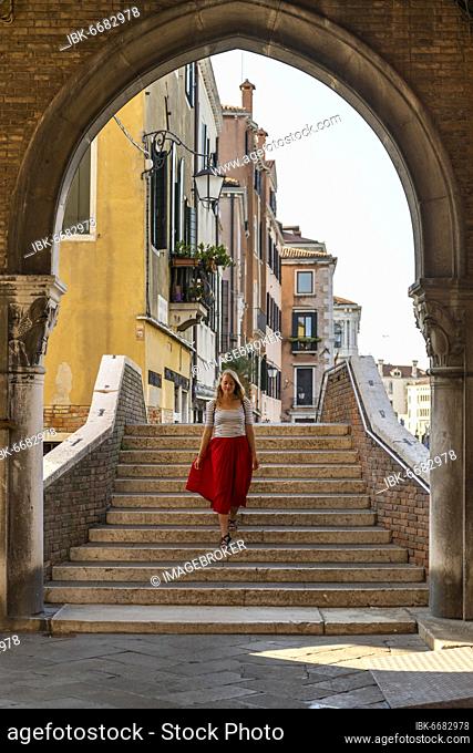 Young woman with red skirt walks through archway, Mercato di Rialto, Venice, Veneto, Italy, Europe