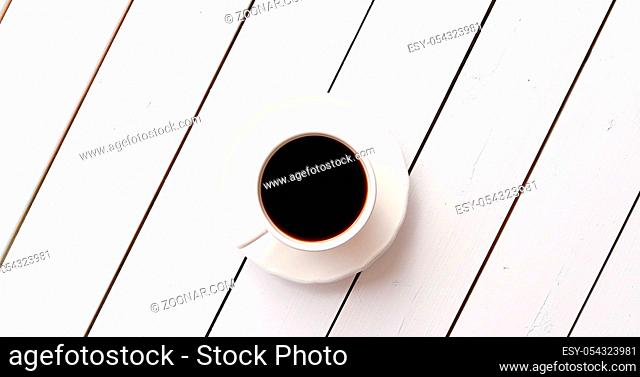 From above shot of cup of fresh hot drink standing on surface of white wooden tabletop