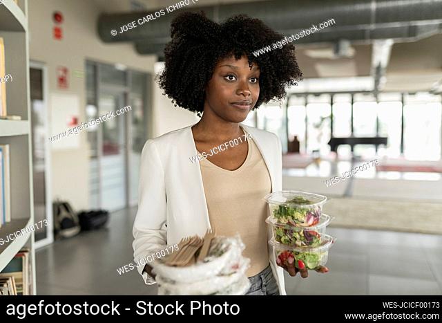 Young businesswoman with salad boxes standing in office