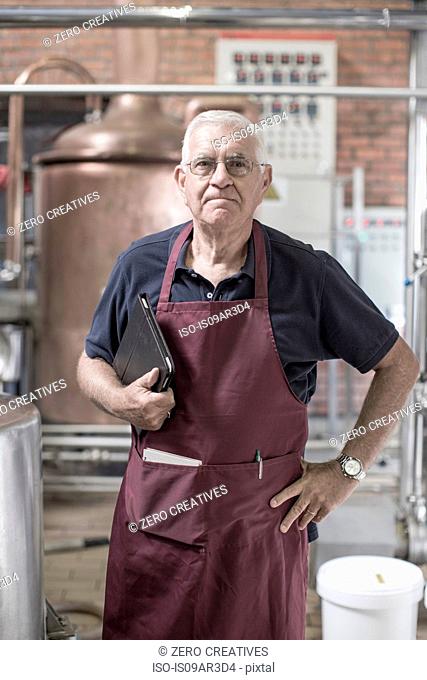 Portrait of brewer in brewery, standing next to stainless steel tanks
