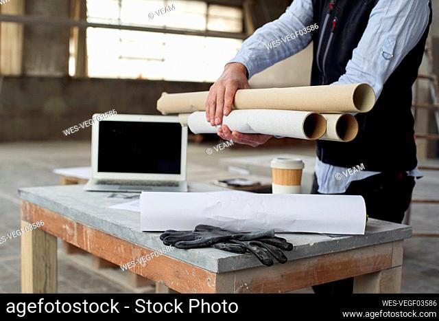 Male architect holding papers while standing at table in building