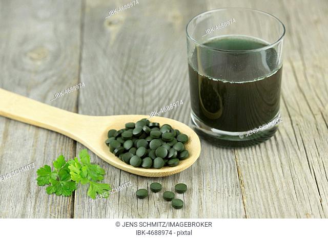 Chlorella, fresh water algae, pellets on wooden spoon with smooth parsley and dissolved in water glass