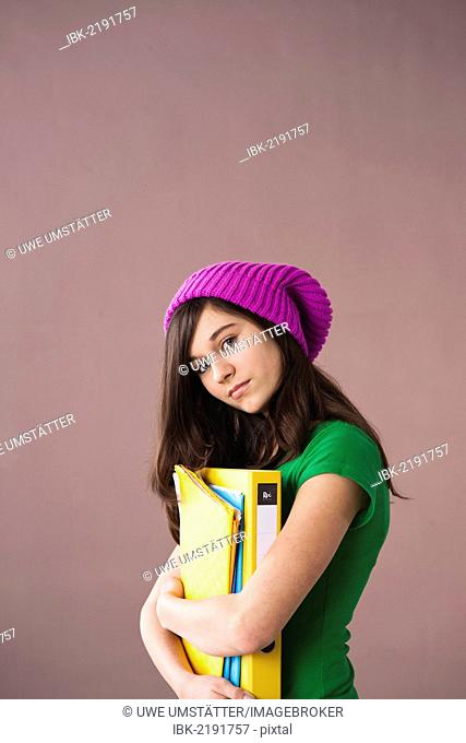 Girl with long hair wearing a hat and holding her school books in her arms