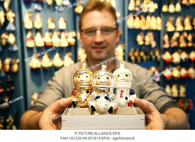 20 December 2018, Thuringia, Lauscha: Glassblower Michael Haberland shows three examples of Christmas tree decorations in the shape of an astronaut