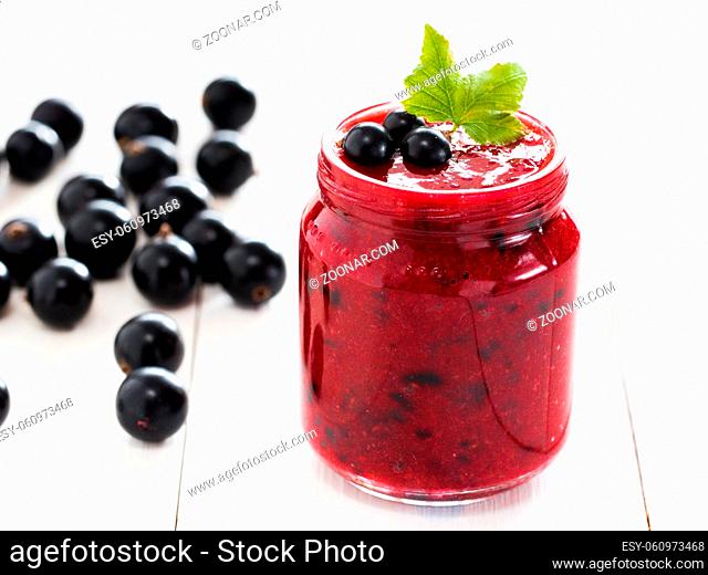 Delicious black currant smoothie or jam in glass jar with fresh berries on white wood background. Shallow DOF. Selective focus