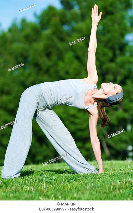 Beautiful woman doing stretching exercise on green grass at park. Yoga