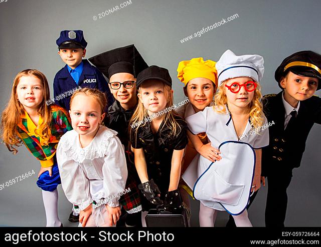 The group of different little children dressed in uniforms of different professions posing on a gray background