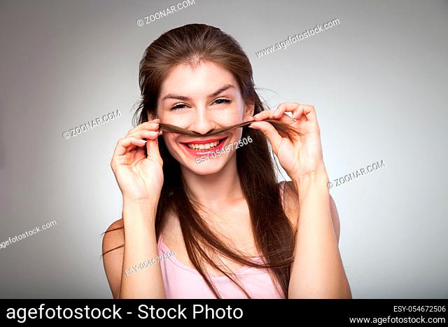 smiling brunette woman holding her hair and showing mustache. Studio shot
