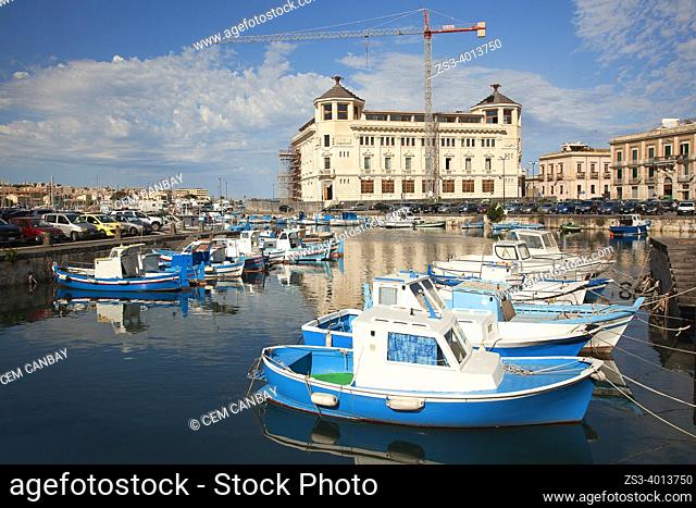 Traditional fishing boats inside the harbor of the Island Of Ortigia with the Post Office Building at the background, Ortigia island, Syracuse, Sicily, Italy