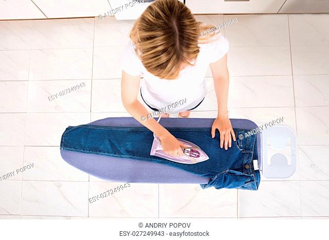 High Angle View Of Young Woman Ironing Jeans On Ironing Board At Home