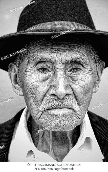 Local black and white image of old man with wrinkles and great eyes against bright wall with black cowboy hat in tourist village of Antigua Guatemala