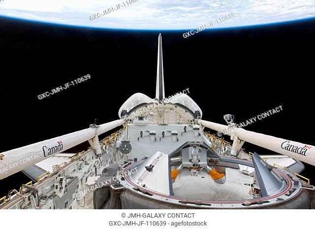 Backdropped by the blackness of space and Earth's horizon, a partial view of Space Shuttle Endeavour's payload bay, docking mechanism, vertical stabilizer