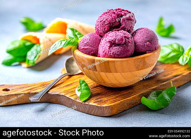 Artisanal blueberry ice cream and green basil in a wooden bowl on a serving board, selective focus