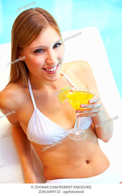 Lächelnde attraktive junge Frau sitzt mit einem Cocktail am Pool