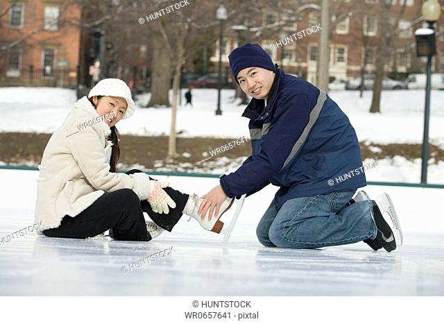 Portrait of a young man tying ice skate laces of a young woman