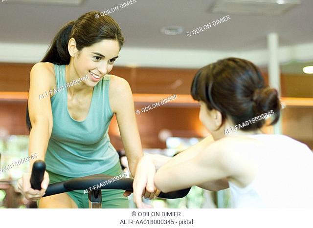Woman riding exercise bike, talking to second woman