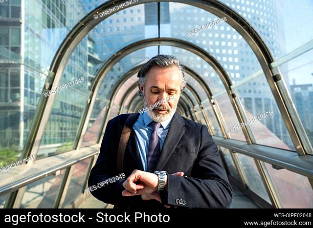 Mature businessman checking time standing on footbridge