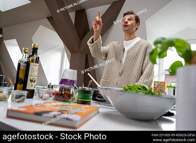 05 October 2023, Bavaria, Munich: National soccer player Thomas Müller speaks and gestures at a stove during the presentation of the cookbook ""Kochen für...