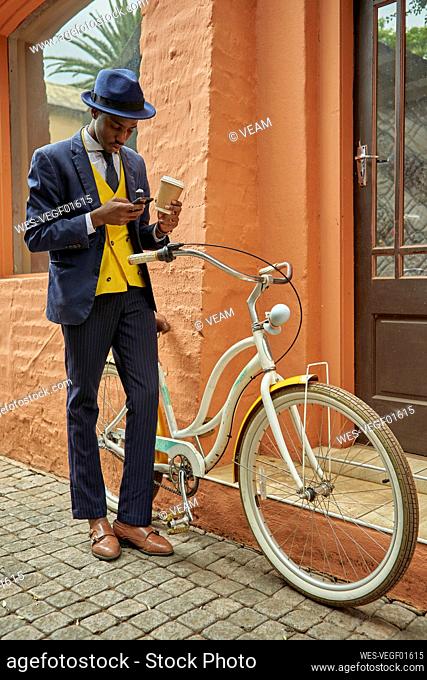 Stylish young businessman with bicycle wearing old-fashioned suit checking his phone