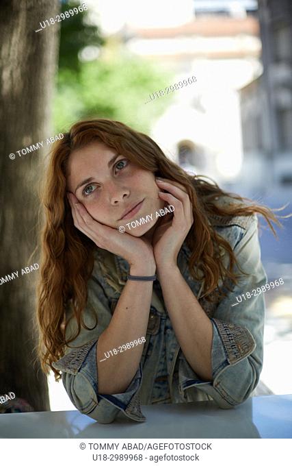 Young redhead woman sitting out with hands in cheek