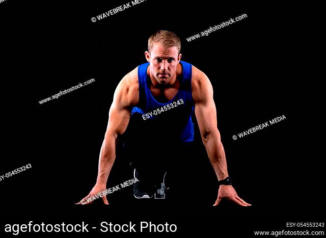 Front view close up of a fit handsome young muscular Caucasian male runner on starting blocks, ready to race on black background