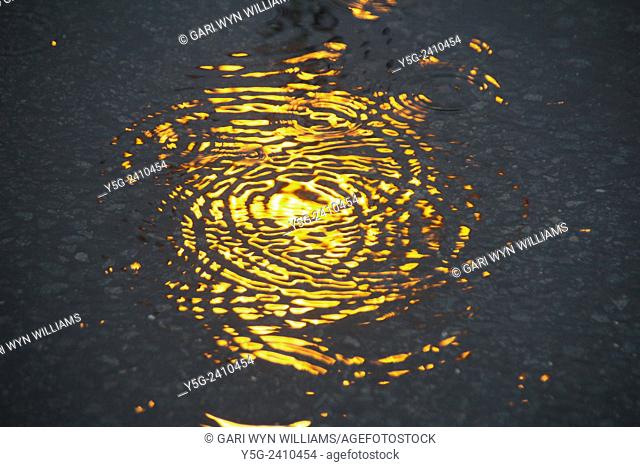 Raindrops falling into a puddle in street road at night