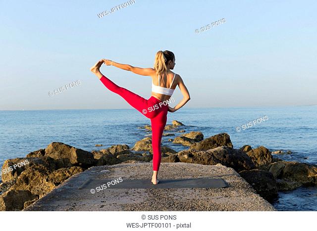 Young woman practicing yoga on the beach, doing standing balance, Utthita Hasta Padangustasana