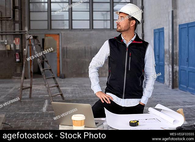 Male architect contemplating while standing at table in building