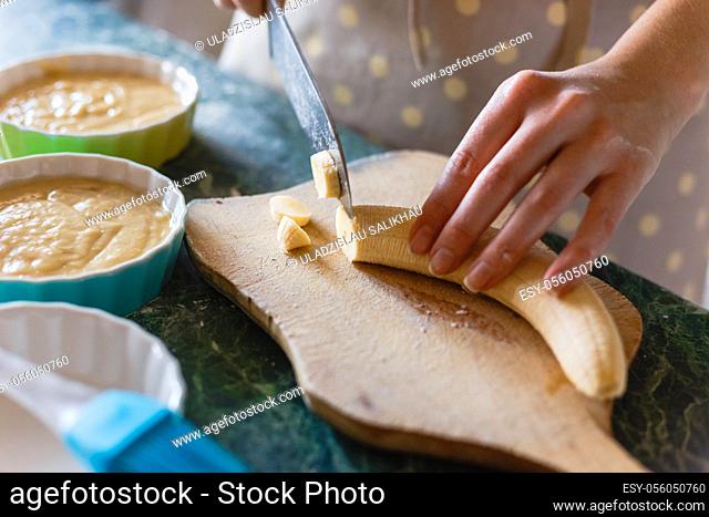 Woman cuts a banana with a knife on rude wooden board