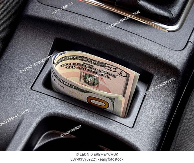 Several banknotes American dollars lie in the niche of the central console of the car. The money in the car