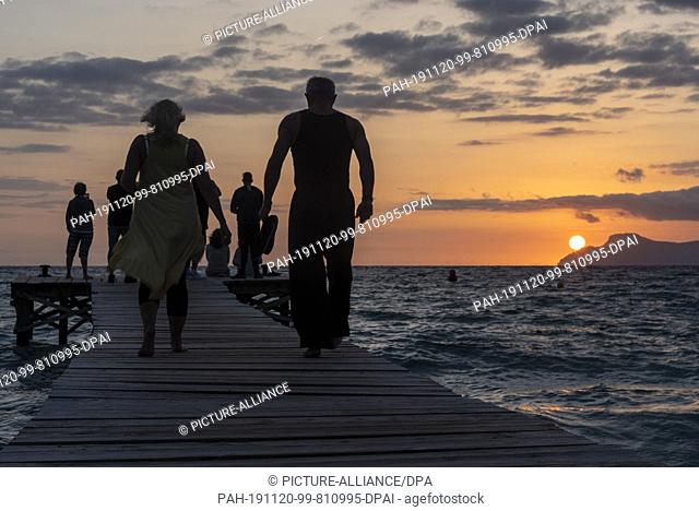 10 October 2019, Spain, Playa De Muro: Tourists photograph and enjoy the sunrise from a jetty at Playa de Muro, the longest sandy beach of Mallorca