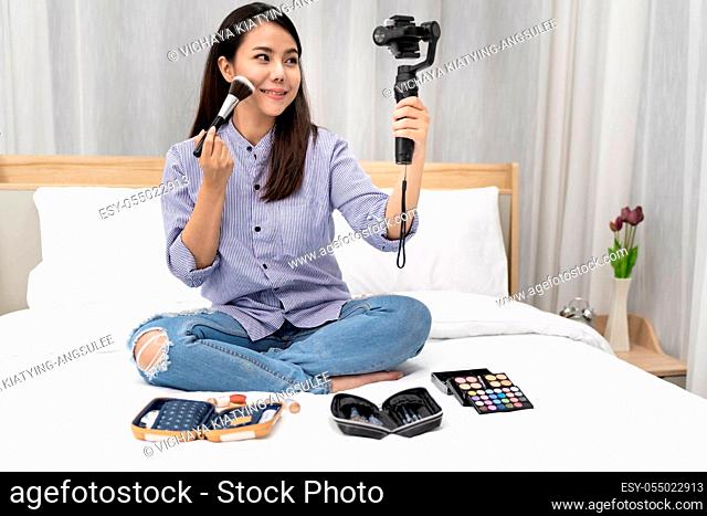 Young beautiful Asian woman beauty vlogger blogger recording live how to make up tutorial to share on social media using Gimbal Stabilizer on mobile phone