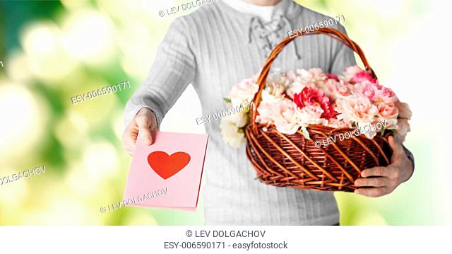 holidays, people, feelings and greetings concept - close up of man holding basket full of flowers and giving postcard over green background