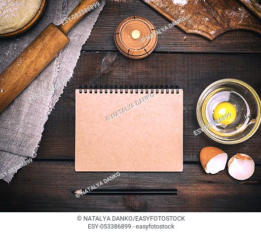 empty paper notebook with brown pages to record a recipe for dough dishes, next to an egg and a kitchen roll, top view