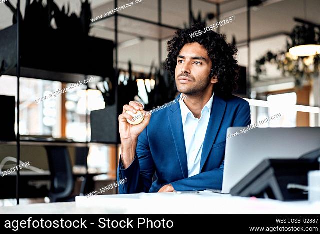 Thoughtful young male entrepreneur looking away while squeezing stress ball at desk in office