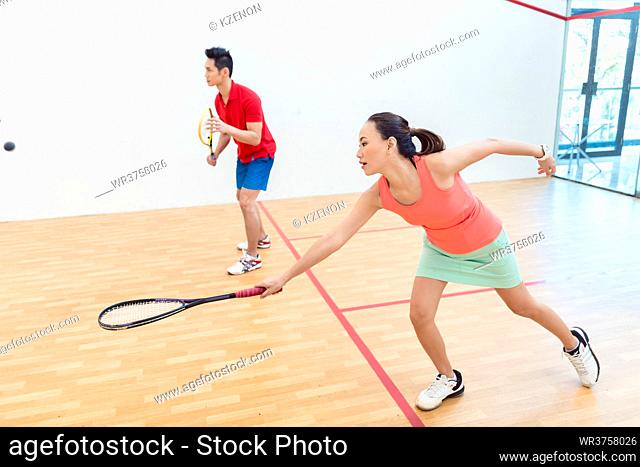 Side view of a beautiful and competitive Chinese woman holding the racquet while looking forward with concentration during a squash game with her partner